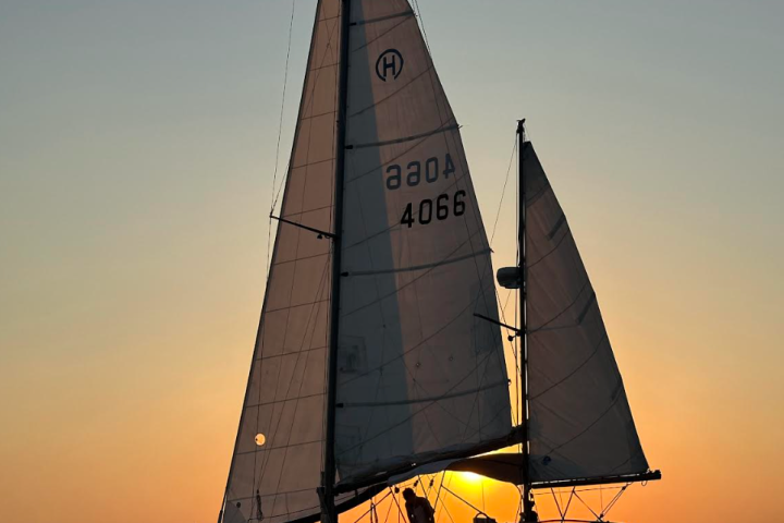 Sailboat on water at sunset with silhouetted sails.