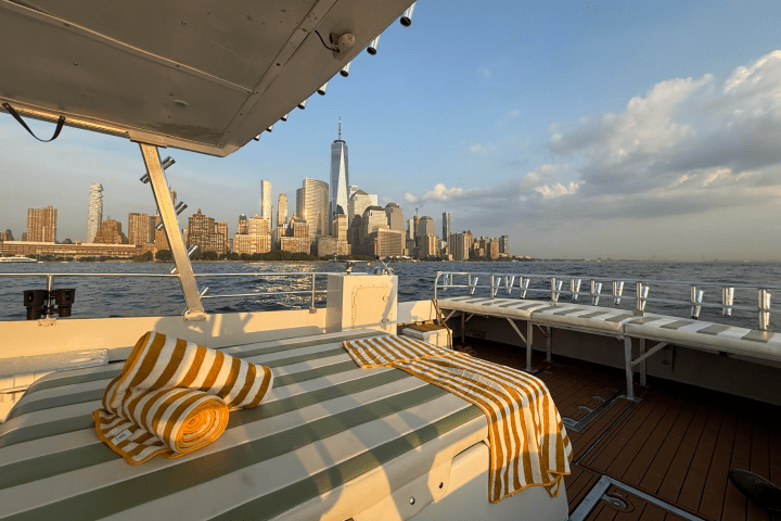 Boat deck with striped towels, city skyline and water in the background at sunset.