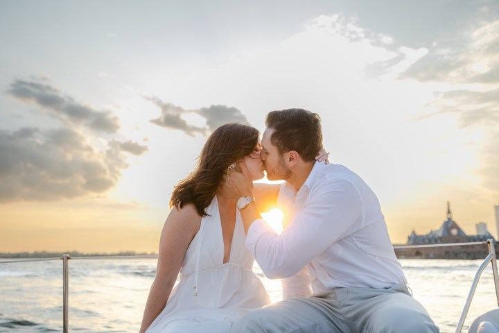 Couple kissing on a boat at sunset, city skyline in background.