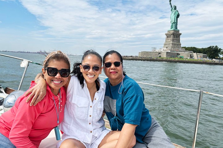 Three people smiling on a boat with the Statue of Liberty in the background.
