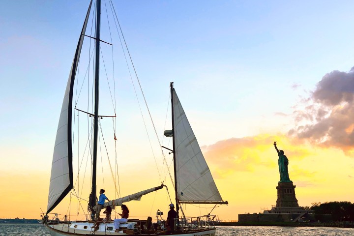 Sailboat on water near the Statue of Liberty at sunset.