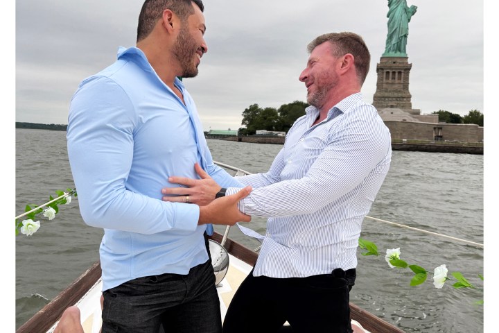 Two people smiling on a boat near the Statue of Liberty with fruit bowl.