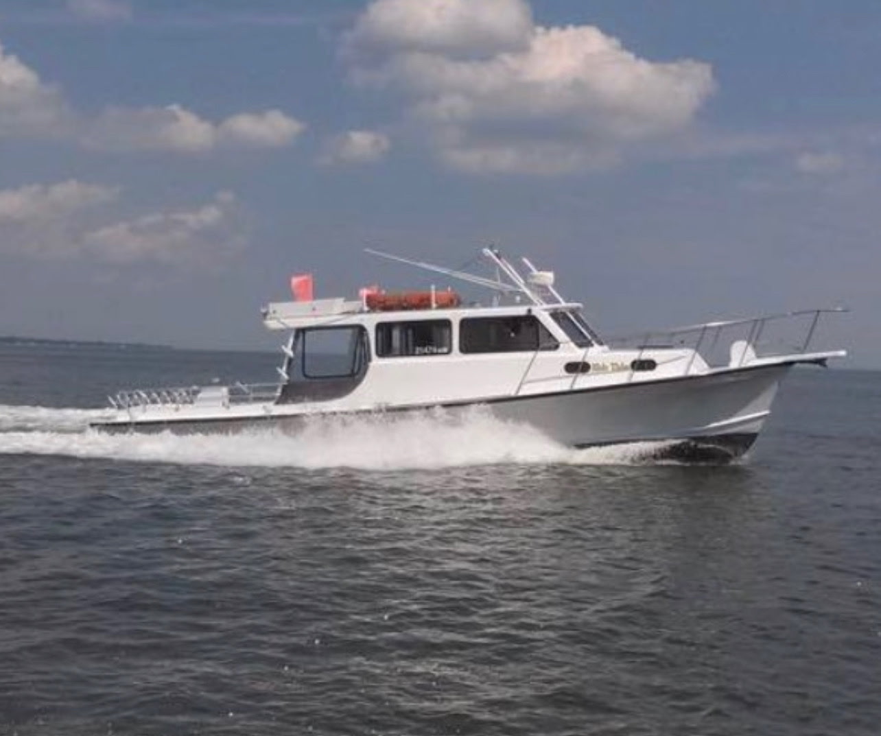 White motorboat speeding on a calm sea under a partly cloudy sky.