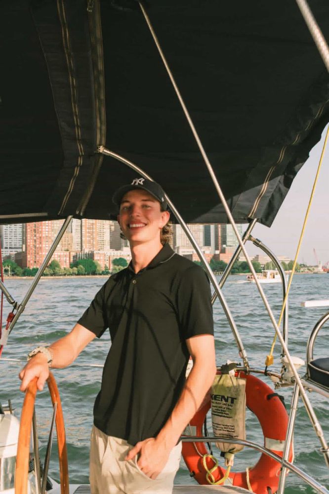 Person smiling on a boat with city skyline in the background.