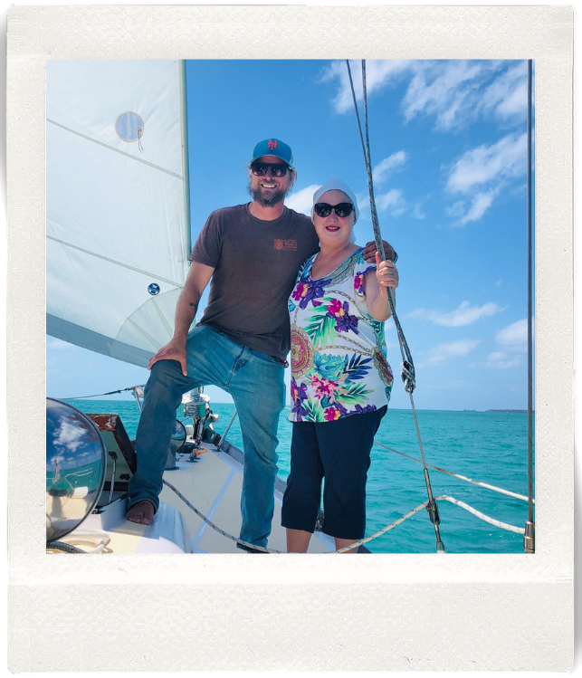 Two people on a sailboat with clear skies and turquoise water.