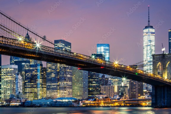 Brooklyn Bridge with a city skyline at twilight, lights reflecting on water.