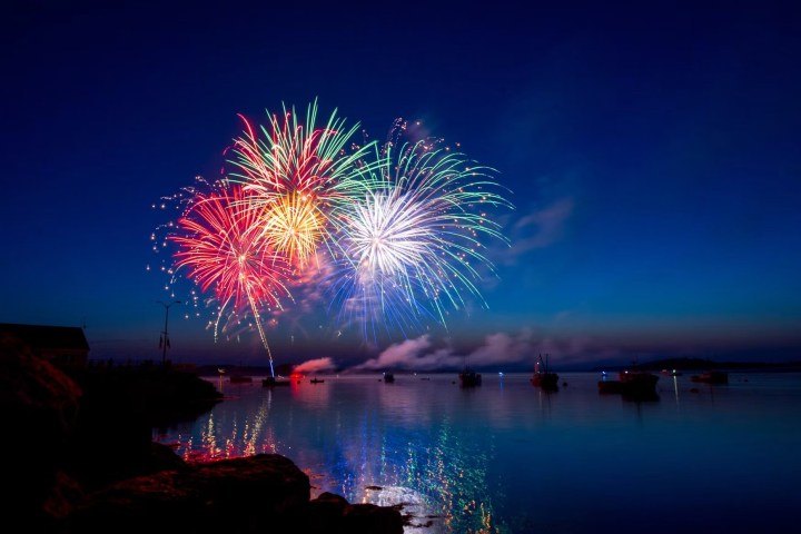 Colorful fireworks over a calm lake at night with reflections on the water.