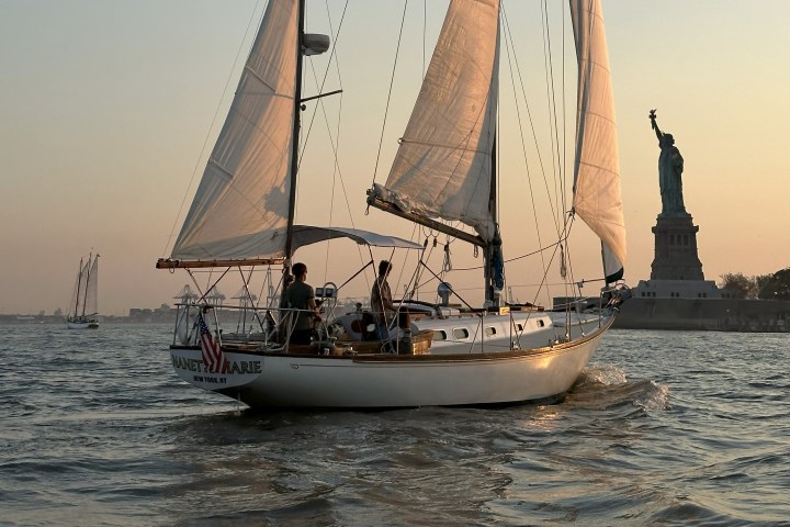 Sailboat on water near Statue of Liberty at sunset.