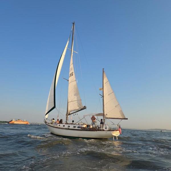 Sailboat with people on open water under a clear blue sky.
