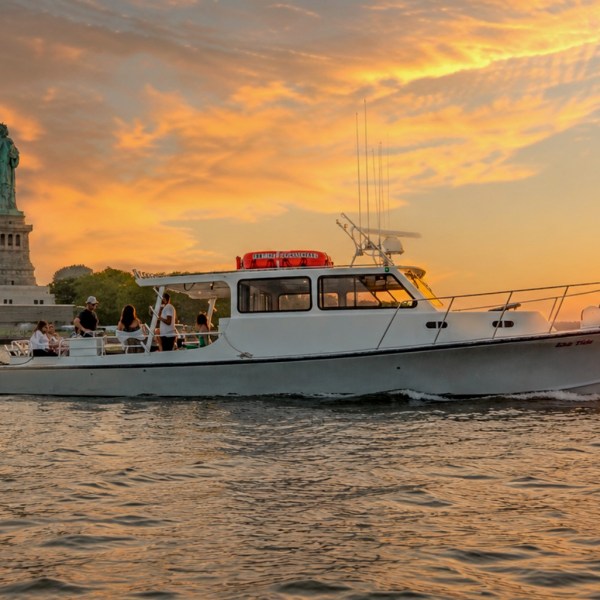 Boat near Statue of Liberty at sunset with orange sky.